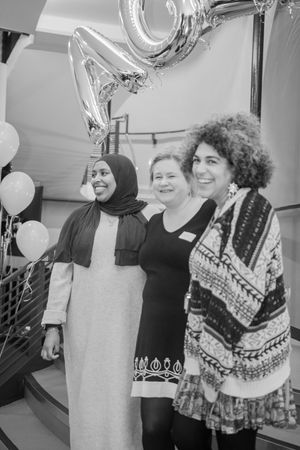 Three women smiling together at a celebration with silver number balloons in black and white photo.