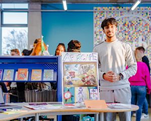 A student stands proudly beside a creative art display in a school library.