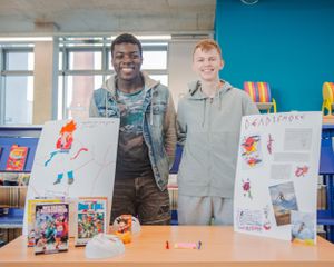Two young men smiling beside comic art project displays on a table.