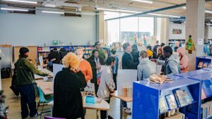 A busy school library filled with students browsing and socializing at displays.