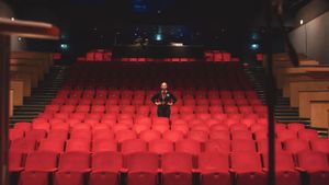 Person standing alone among rows of empty red theater seats in a modern auditorium.