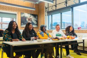 Diverse group of five people sit together at a long white table in a modern brick-walled room.