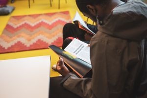 Student reading a book at a colorful classroom desk with a vibrant chevron rug in the background.