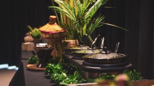 Elegant African-themed food buffet display with warm dishes, tropical plants, and woven decorative baskets.