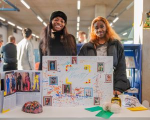 Two young women standing proudly behind a colorful creative project display.