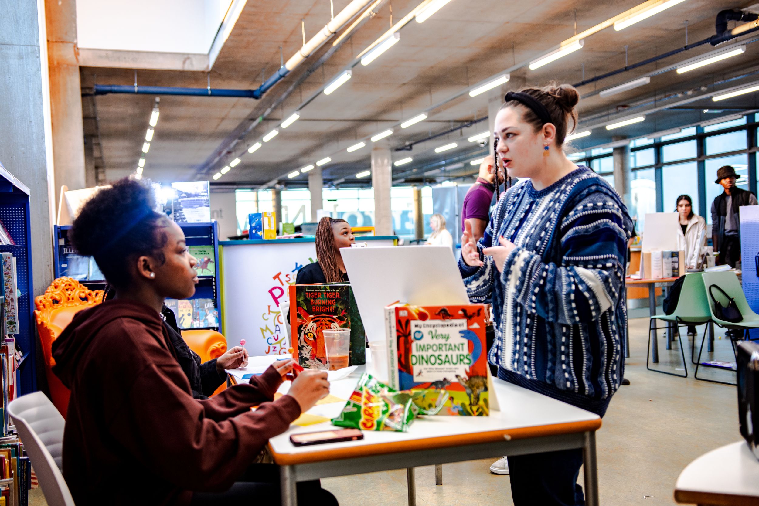 Two students discuss a colorful book display in a bright school library.