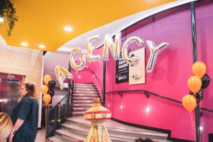 Vibrant pink and yellow venue entrance decorated with silver AGENCY letter balloons and orange balloons.