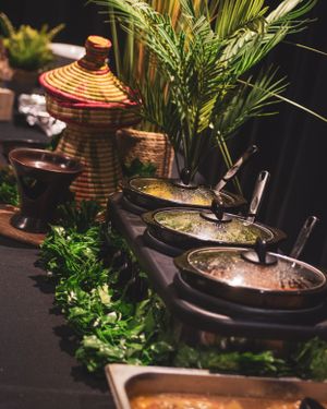 Colorful African buffet spread with warm dishes, fresh herbs, and decorative woven baskets on a dark table.