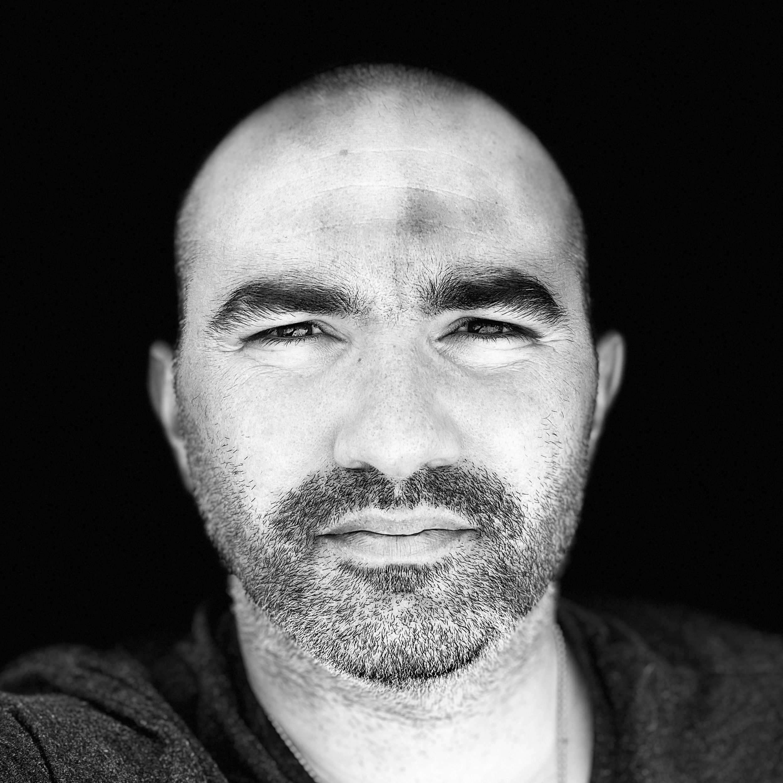 Black and white close-up portrait of a bald middle-aged man with a beard looking at the camera.