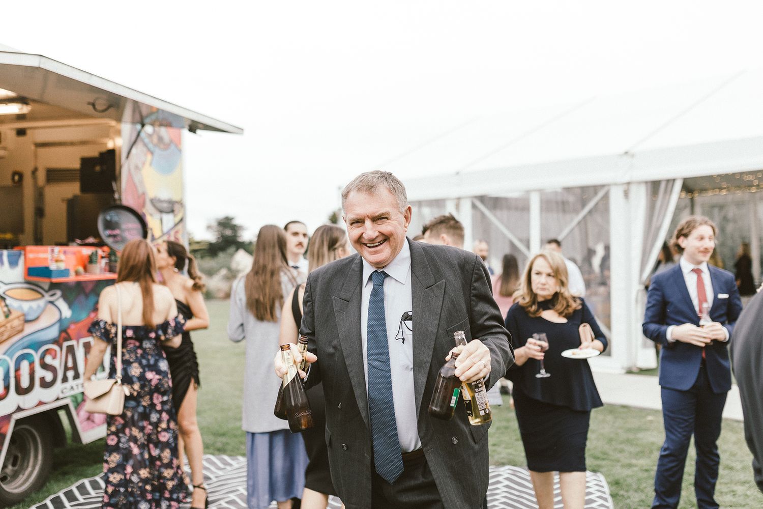 Wedding guests enjoying an outdoor celebration beneath a white tent with a food truck in the background.