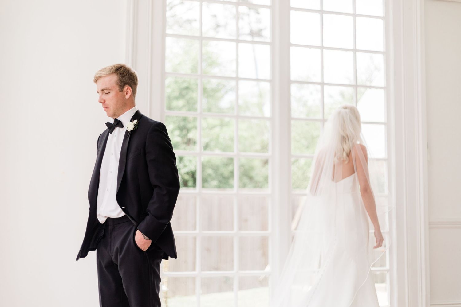 First look wedding moment in bright sunlit room with large windows.