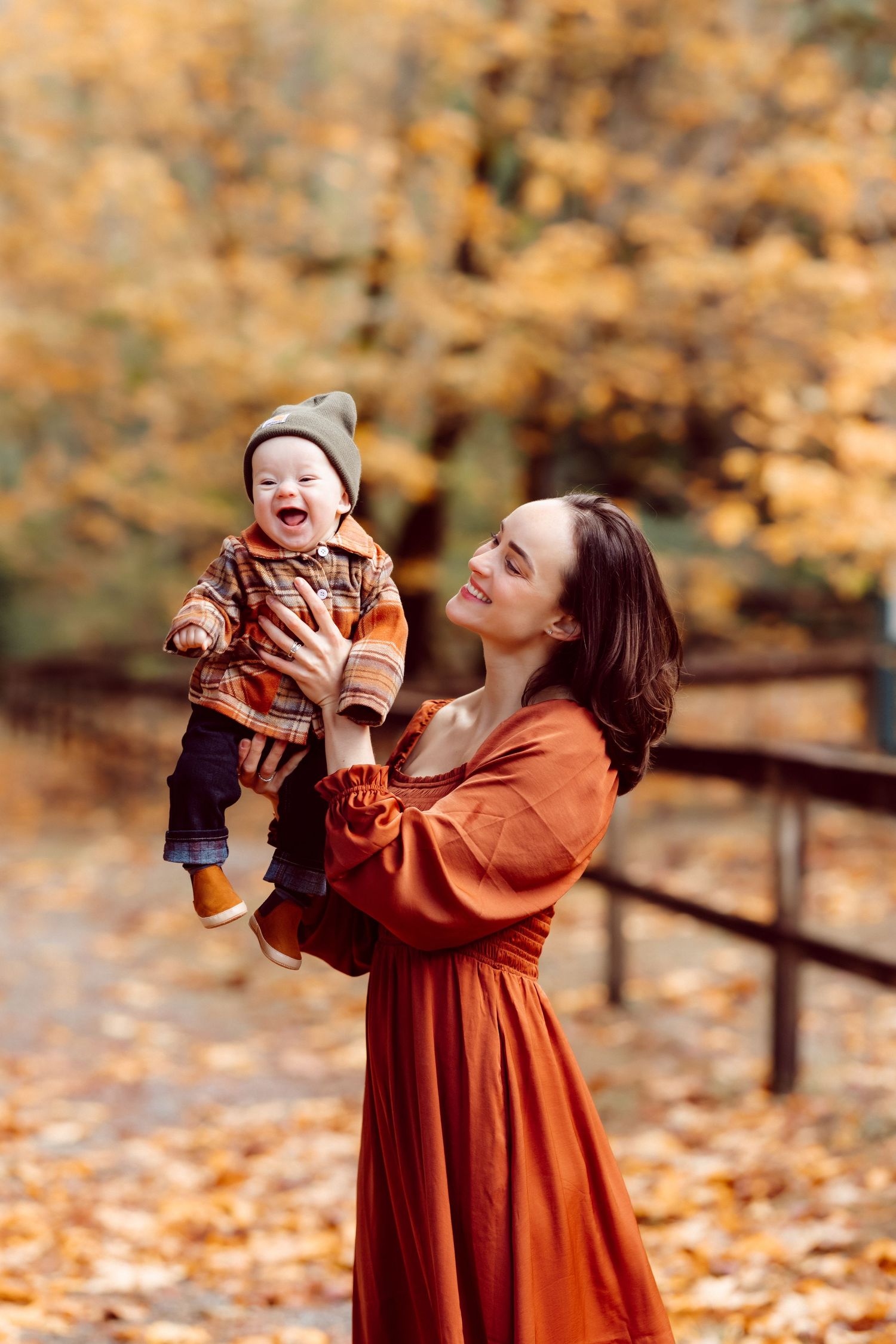 A parent and baby share laughter in an autumn setting with orange leaves.