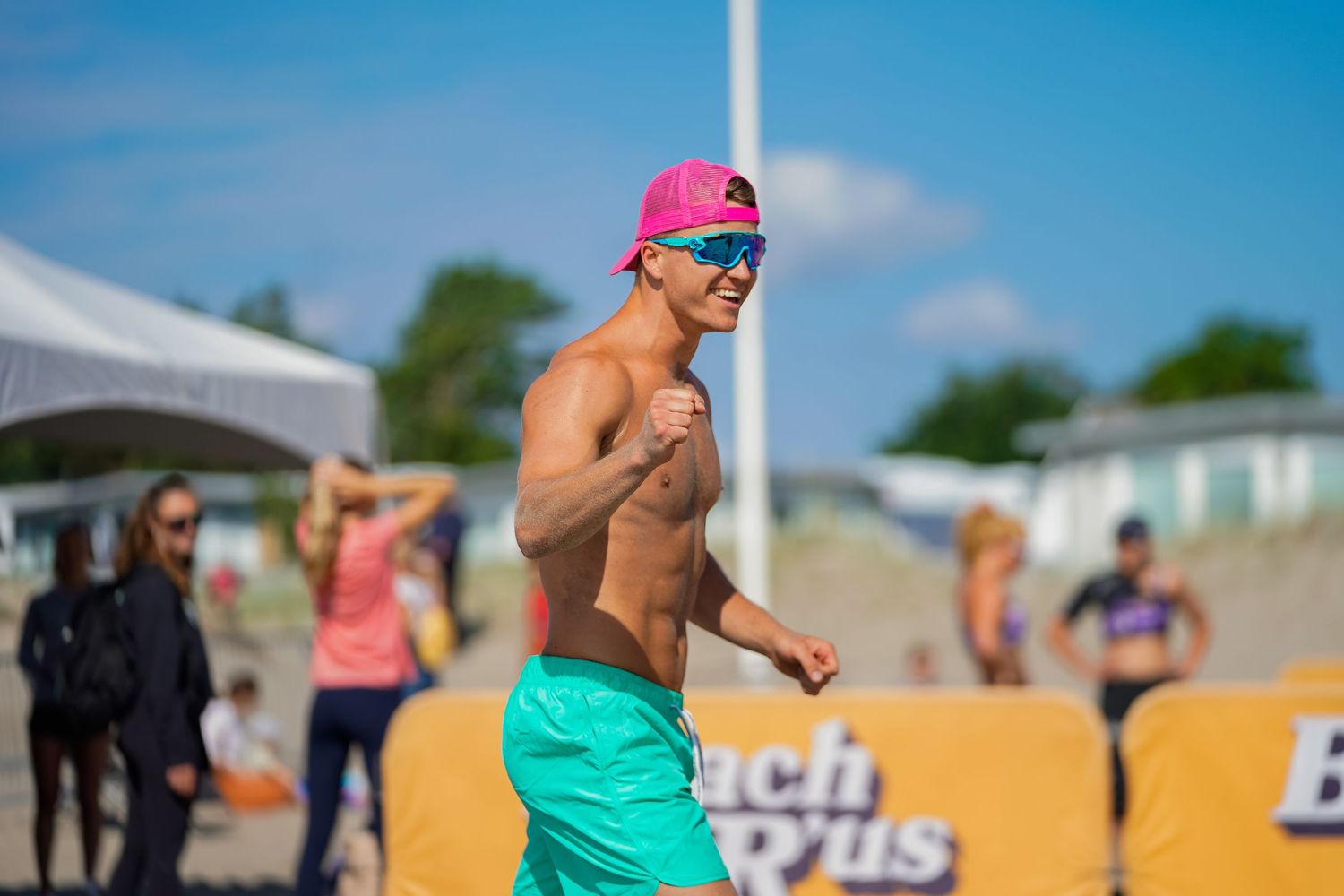 An athlete in teal shorts celebrates during a beach volleyball tournament on a sunny day.