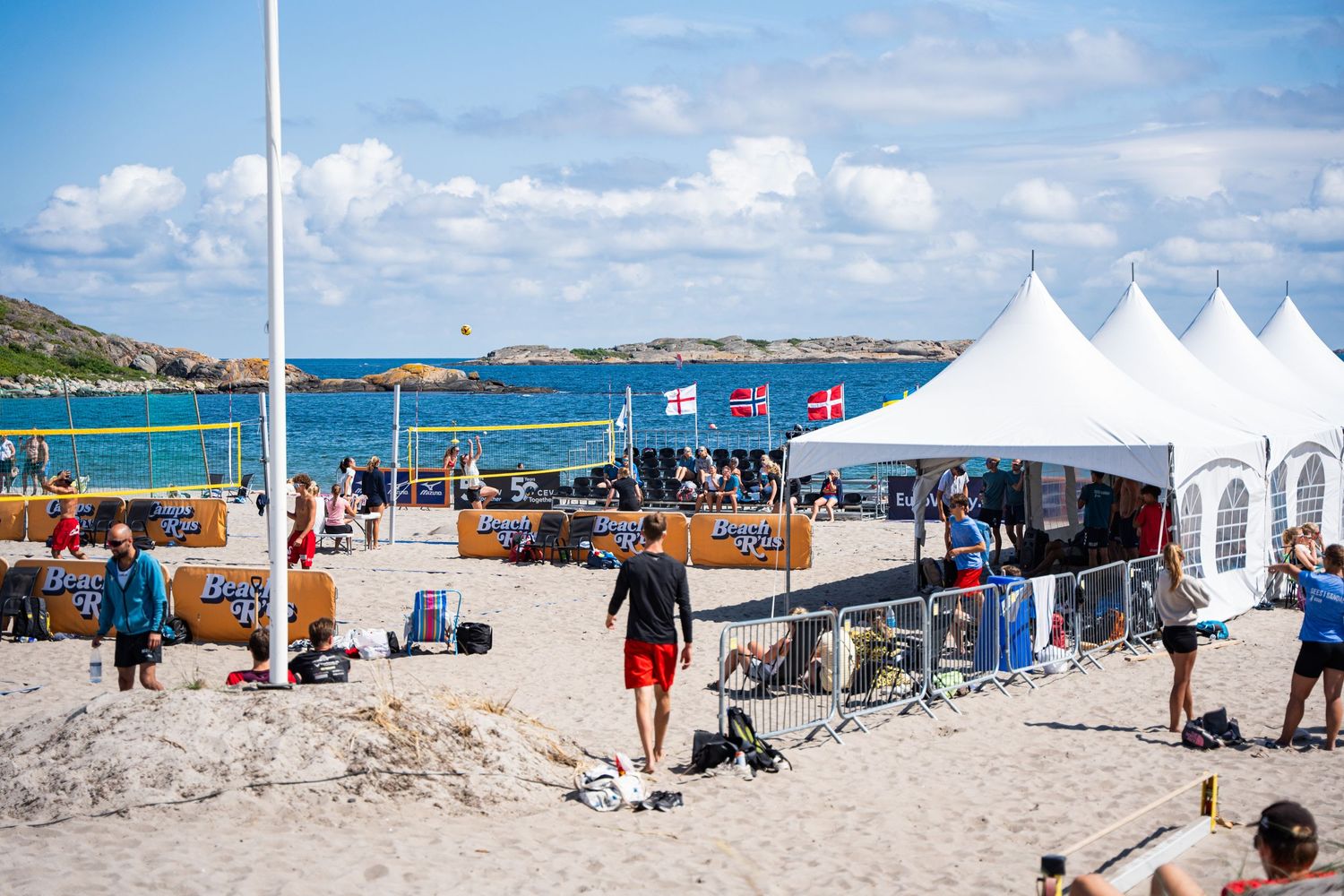 Beach sports event setup with white tents and equipment on sandy shore overlooking ocean.