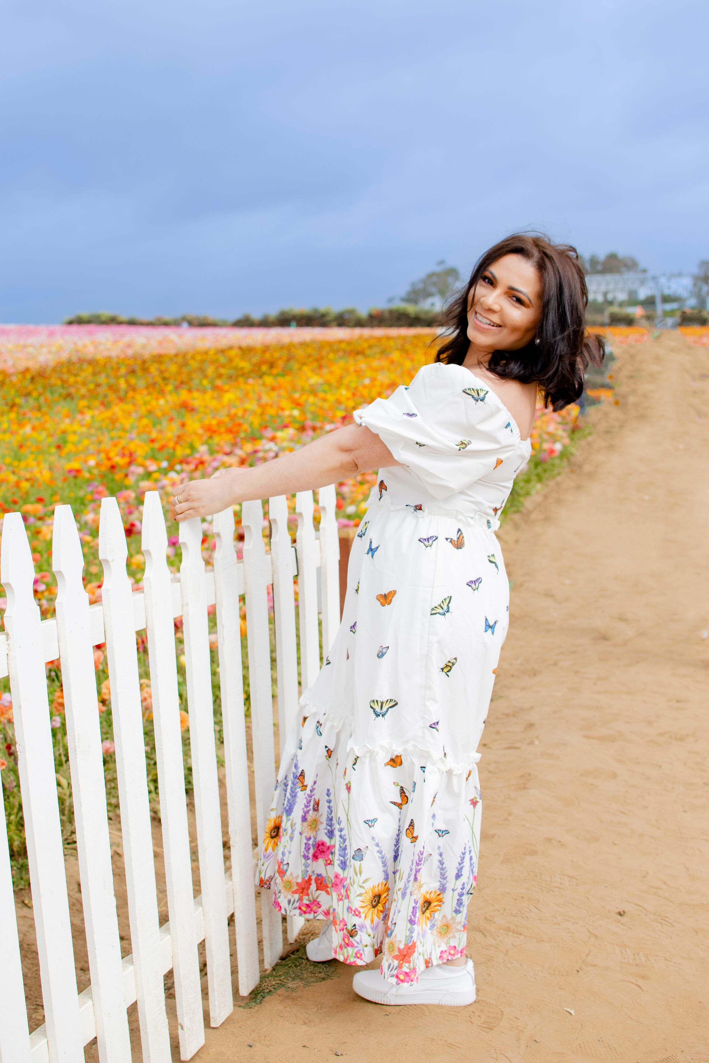 A dreamy portrait in a white dress against a field of wildflowers and white picket fence.