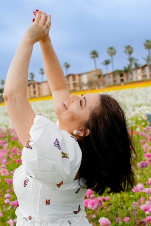 A person wearing a white butterfly dress stretches their arms up while posing in a flower field.