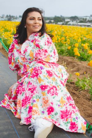 A person in a bright floral dress sits along a path bordered by yellow flowers.