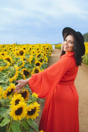 A flowing red dress and black hat create dramatic poses in a sunflower field.