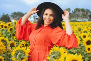 A joyful moment captured in a sunflower field wearing a bright orange dress and wide-brim hat.