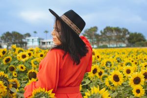 A stunning orange dress creates contrast against bright yellow sunflowers in full bloom.