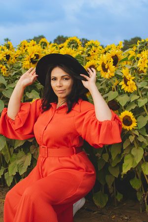 A flowing red dress creates beautiful contrast against yellow sunflowers in a field.