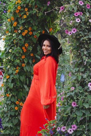 Person in bright coral dress poses against climbing vines with pink and orange flowers.