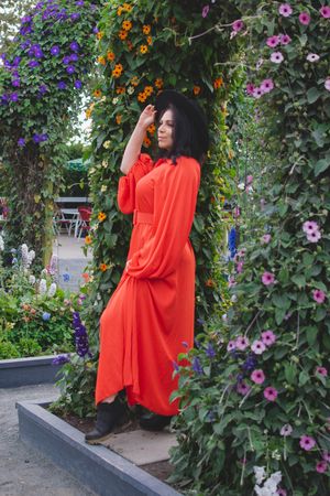 Figure in flowing red dress stands elegantly among purple and pink garden flowers.