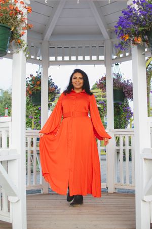 Person wearing long orange dress stands in white garden gazebo with purple flowers.