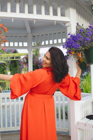 Back view of person in coral dress with bell sleeves posing in white gazebo with flowers.