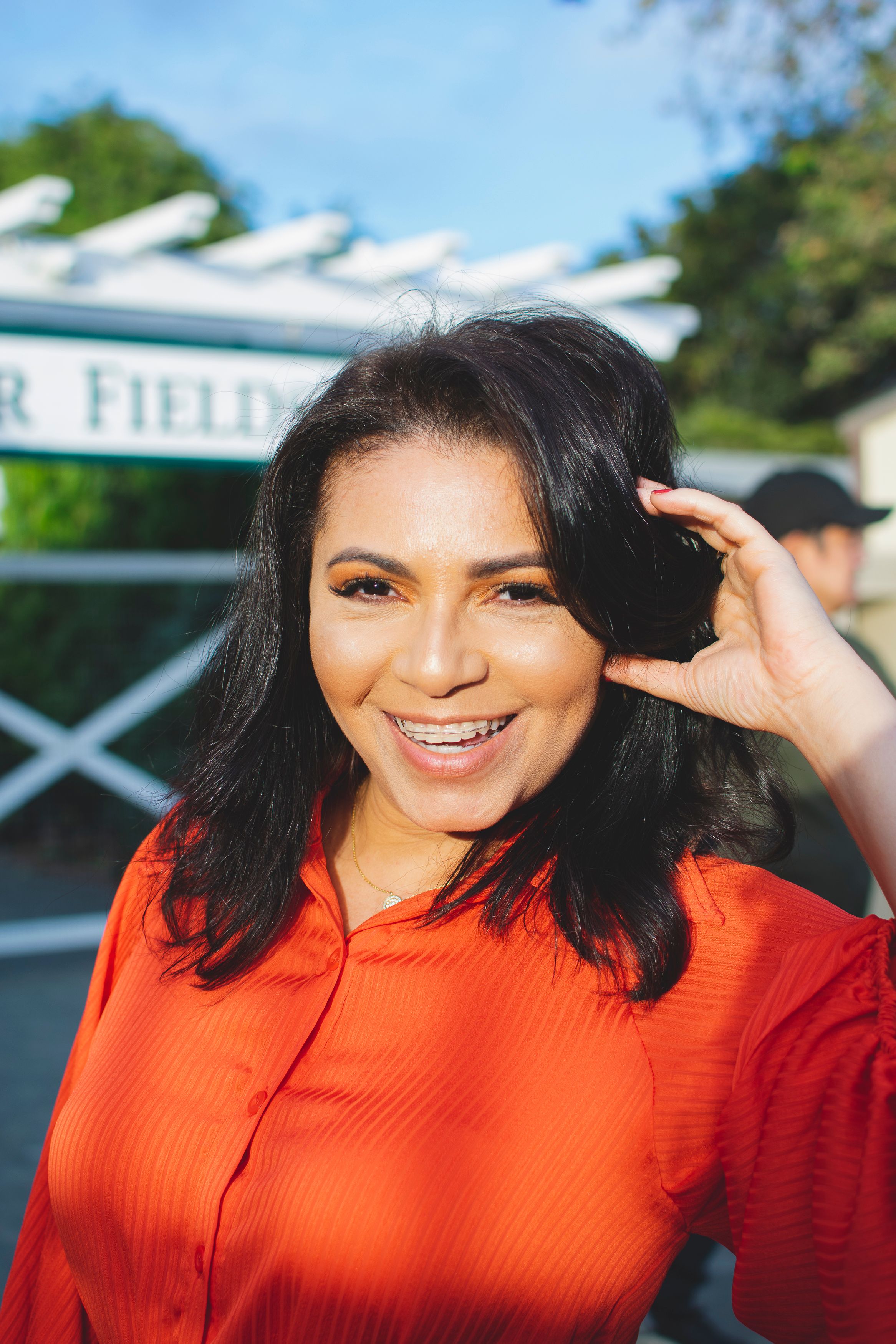 A sunny outdoor portrait featuring a bright orange dress and natural makeup look.