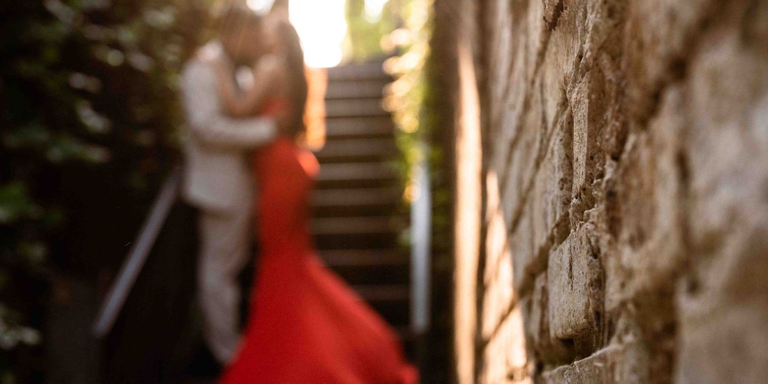 Sun-kissed glow illuminates brick wall, while an out-of-focus couple shares a passionate kiss in the enchanting alleyway