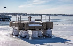 Concrete blocks and barriers line a frozen marina waterfront under bright winter sky.