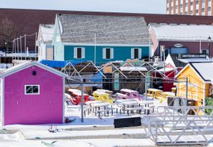 Colorful fishing shacks and buildings line a snowy marina dock in winter.