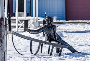 Black metal benches sit empty along a snowy waterfront path.