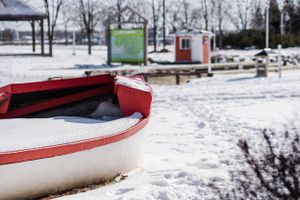 Red and white boats rest on snowy ground near a waterfront.