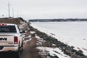 Snow-covered rocky shoreline with vehicles parked along winter waterfront.