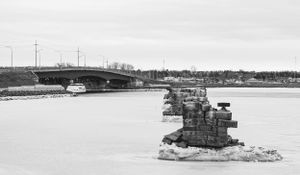 Stone bridge supports stand in frozen water with utility poles and infrastructure visible in winter landscape.