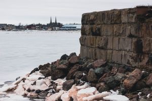 Stone wall and rocky shoreline along frozen waterfront with church spires visible in background.
