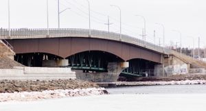 Brown concrete bridge spans across frozen waterway in winter urban setting.