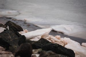 Dark rocks contrast against snow and ice along a frozen shoreline.