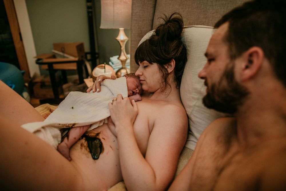mother holds newborn to chest while dad looks at the mess of meconium birth photographer portland oregon