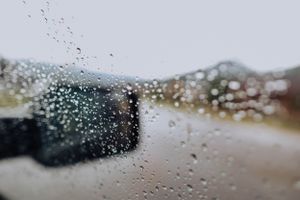 Raindrops on a car window with blurred mountain landscape in the background.