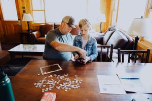 People working on a jigsaw puzzle at a wooden table in a cozy indoor setting.