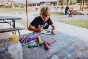 Children engage in creative art activities at outdoor tables in a sunny playground setting.