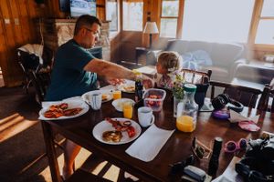 People enjoying breakfast at a rustic wooden table in a cabin setting with sunlight streaming in.