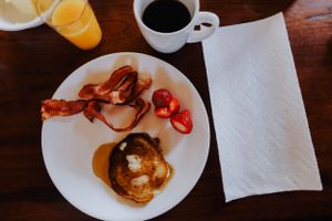 A breakfast plate with bacon and pancakes served alongside coffee and orange juice on a wooden table.