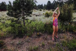A person strikes a joyful pose against a backdrop of desert vegetation and pine trees.
