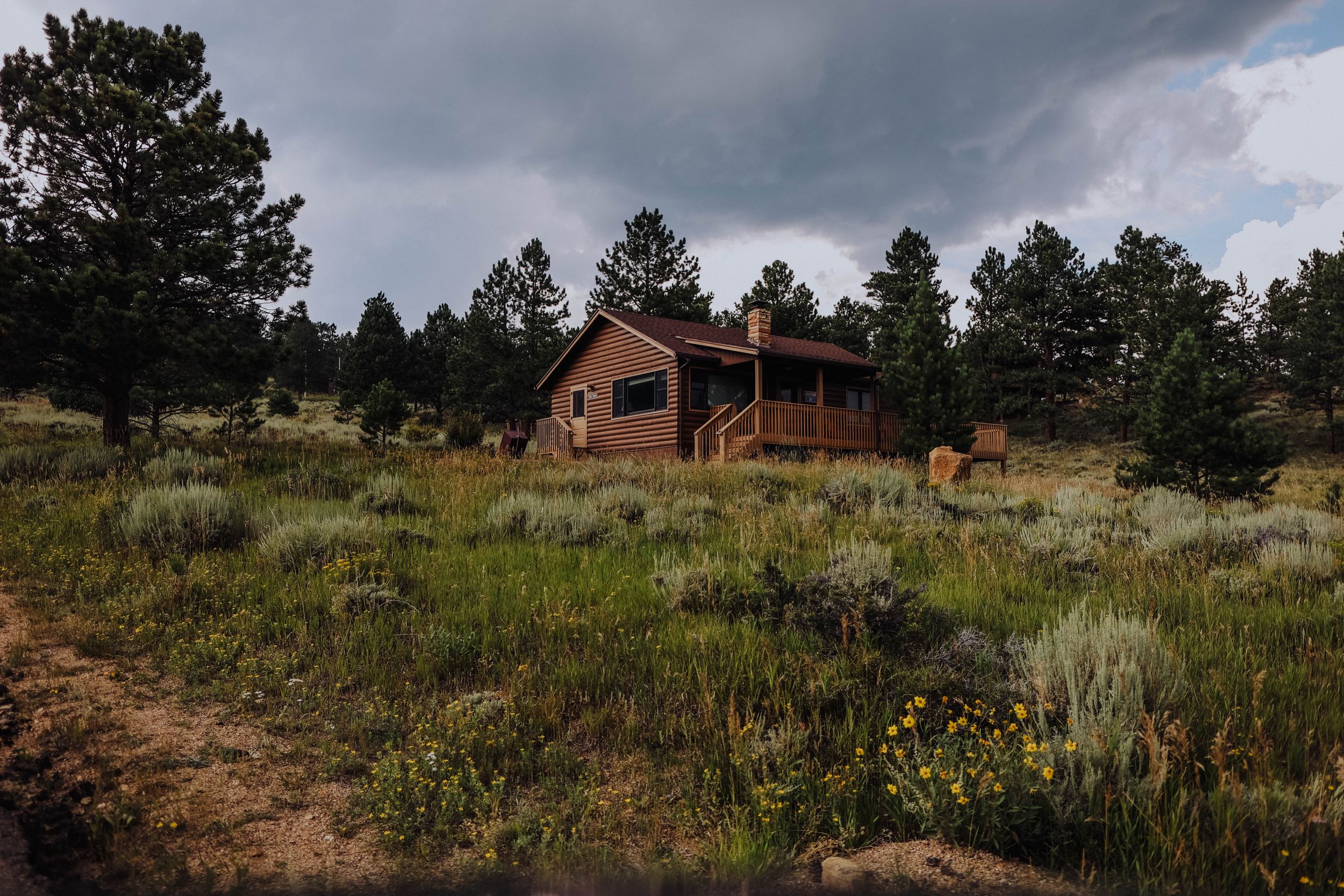 Mountain vista with pine trees and rustic buildings under stormy skies.