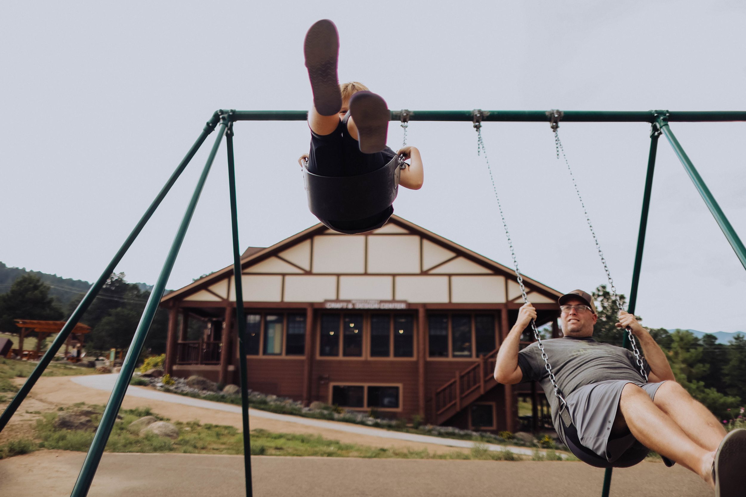 People swinging on playground swings with a building visible in the background.