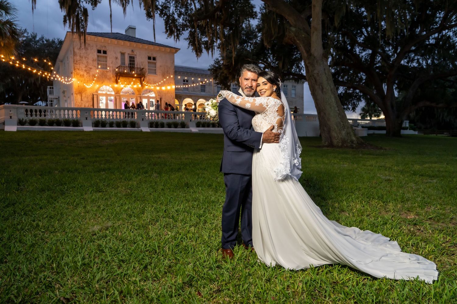 A wedding couple dances at night with a beautifully lit historic building in the background.